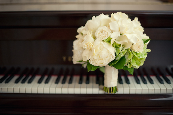 beautiful ivory and green floral bouquet wrapped with ivory ribbon sitting on top of piano keys - photo by Houston based wedding photographer Adam Nyholt 